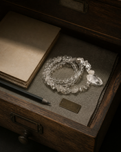 Load image into Gallery viewer, NORBU OBJECTS product image direction: a neck-worn line with a central pendant or focal detail; clear and translucent tones; deep highland light; a map archivist in a quiet Lhasa guesthouse; collector archive.